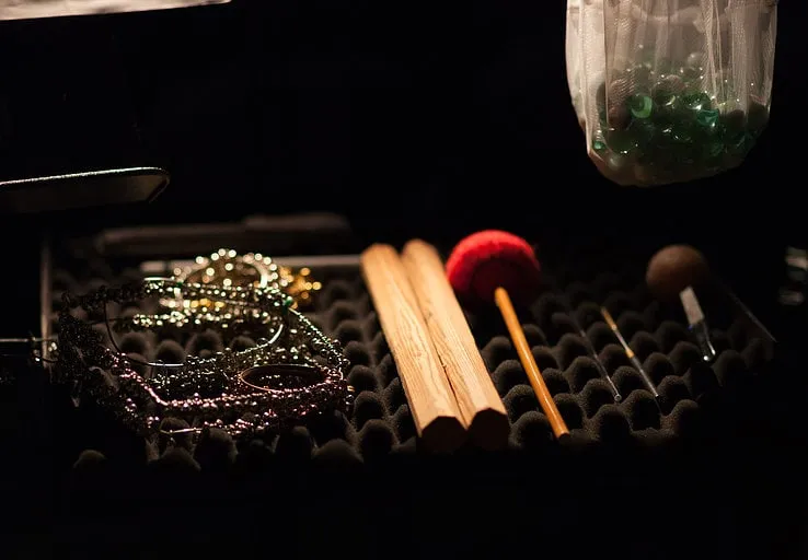 Closeup of assorted wooden, metal and glass percussion instruments sitting on a tray in a dimly-lit performance space.